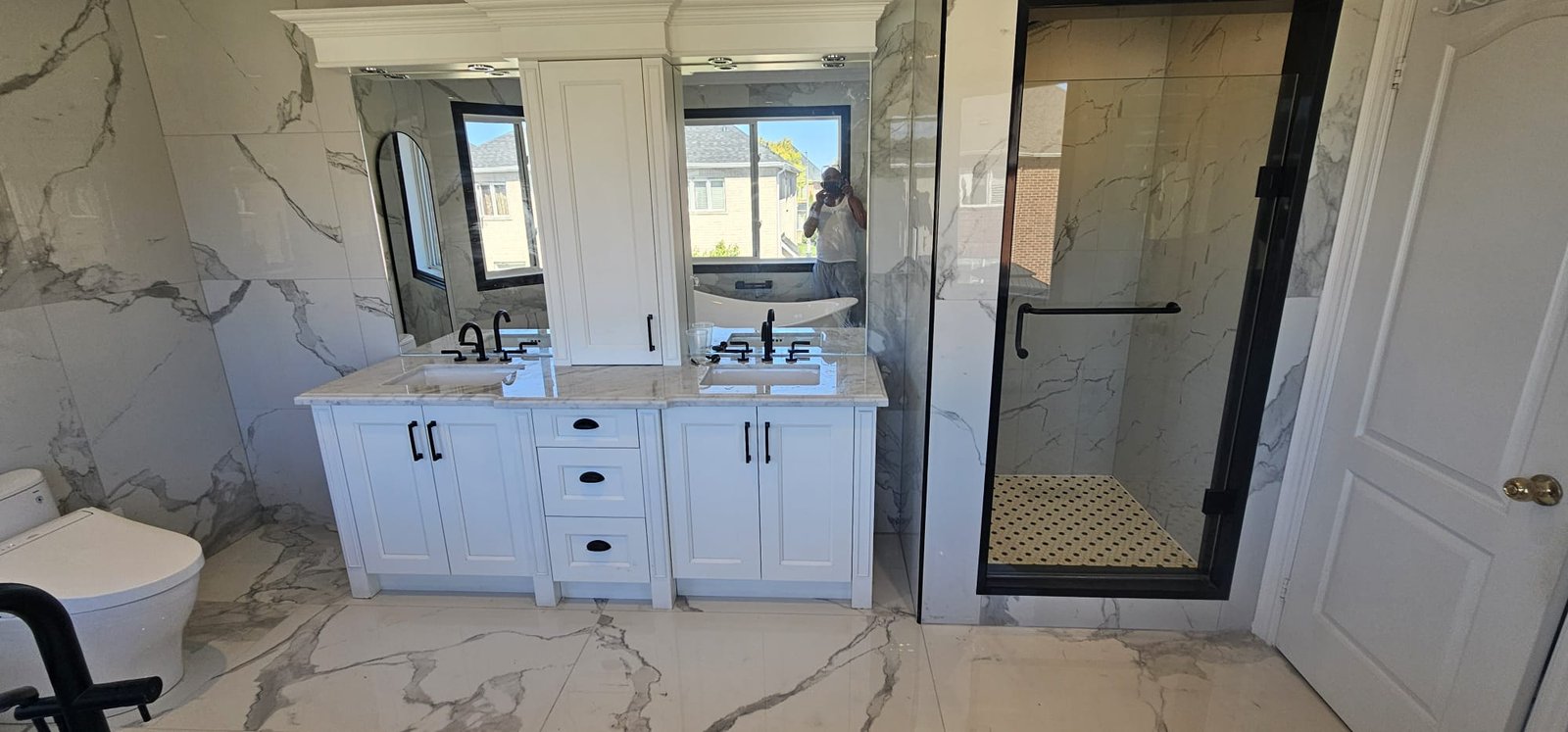 Double vanity bathroom with marble walls and glass shower enclosure