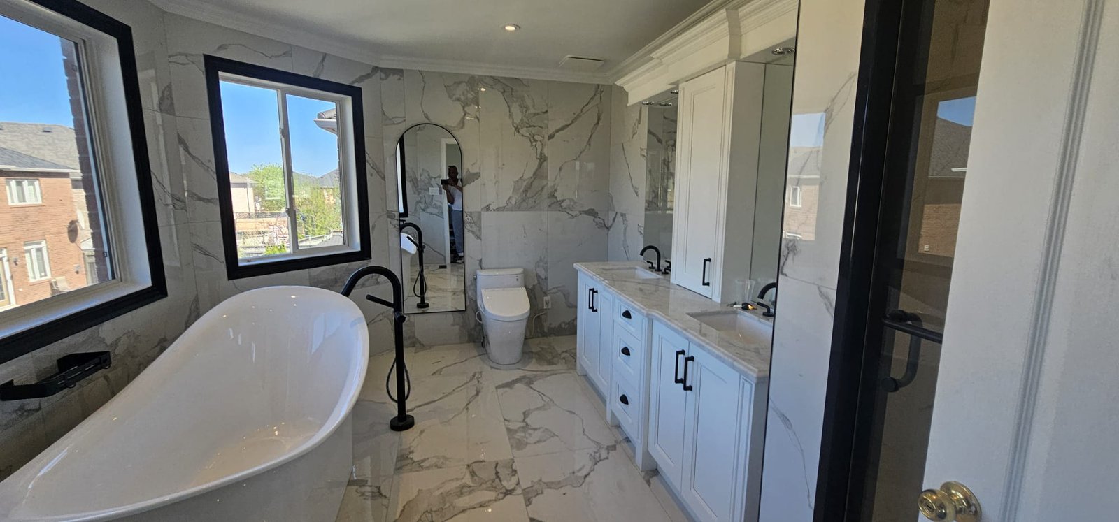 Luxury freestanding soaker tub with marble tile surround and large windows
